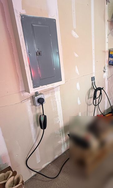 Garage panel with a new EV outlet below it and a charging cable plugged in β Zion Electric Inc., San Leandro electrician